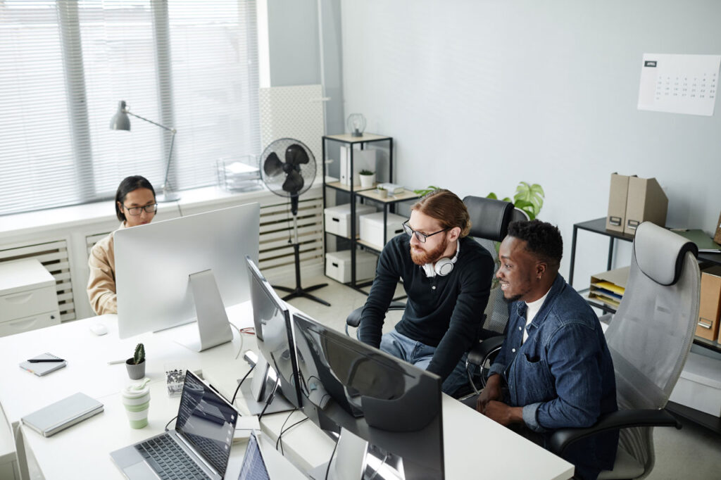 PHP-Entwickler arbeiten gemeinsam an Computern in einem modernen Büro mit mehreren Monitoren und Büromaterialien.